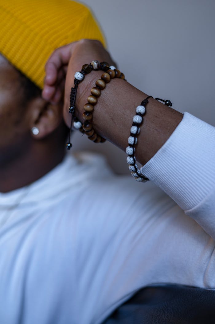 Stylish close-up of beaded bracelets on an arm, wearing a white sleeve and a yellow hat.