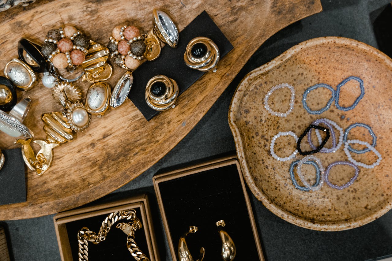 Top view of assorted handmade earrings, rings, and bracelets on ceramic and wooden trays.